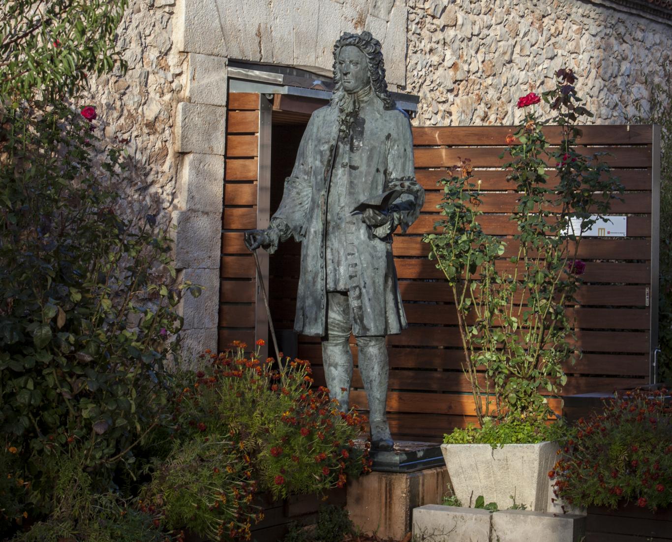 Fachada de un edificio de piedra con una estatua de un hombre del siglo 18