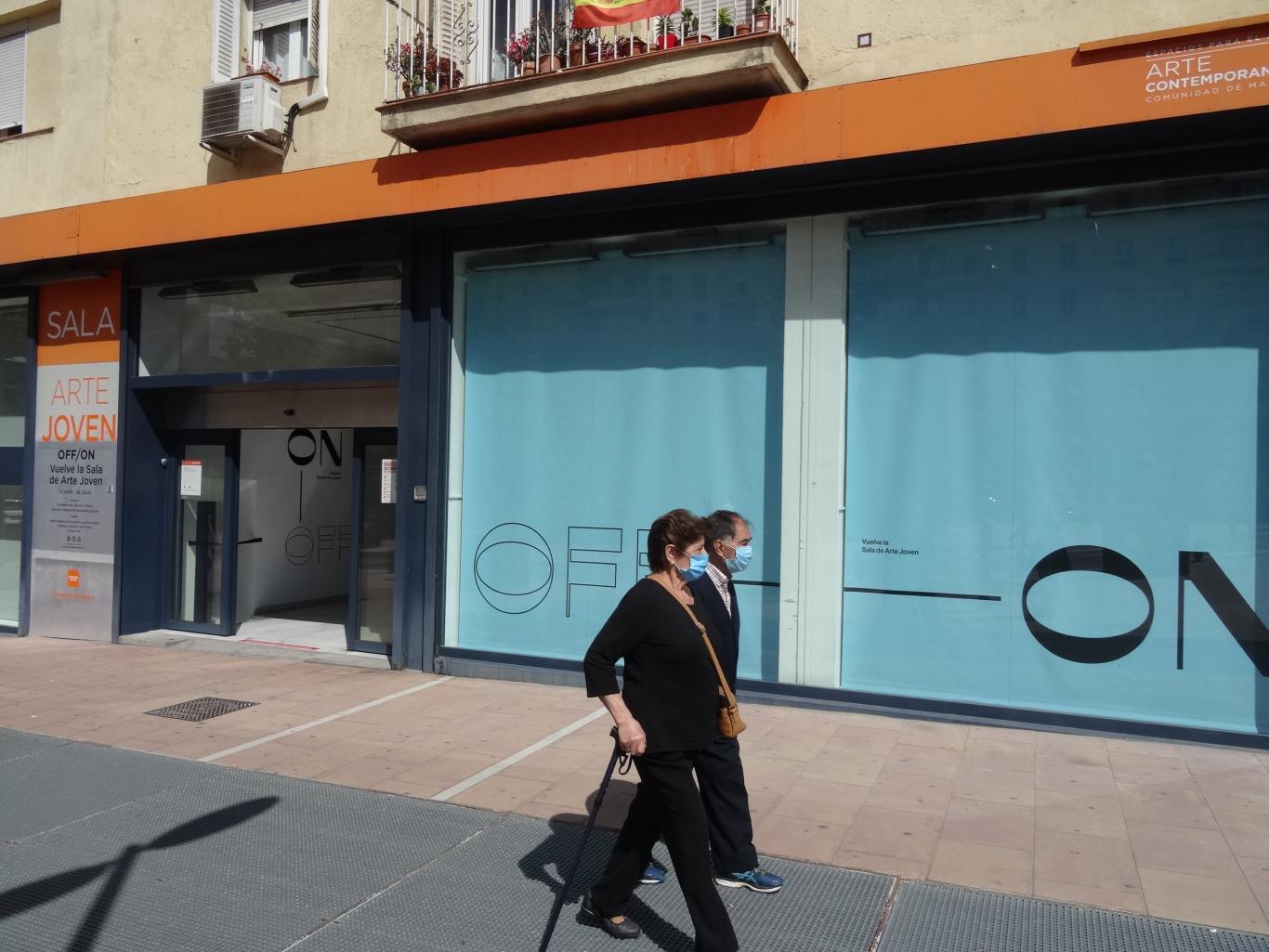 Dos personas con mascarilla pasando por delante de la cristalera de la Sala de Arte Joven