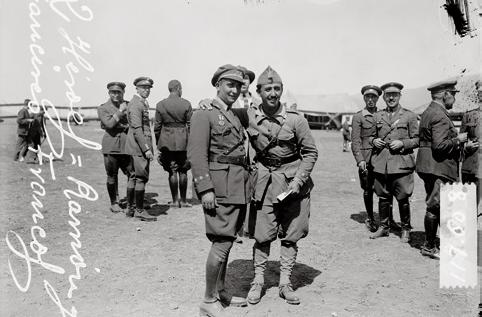 2 militares posando para la foto, observados por otros militares