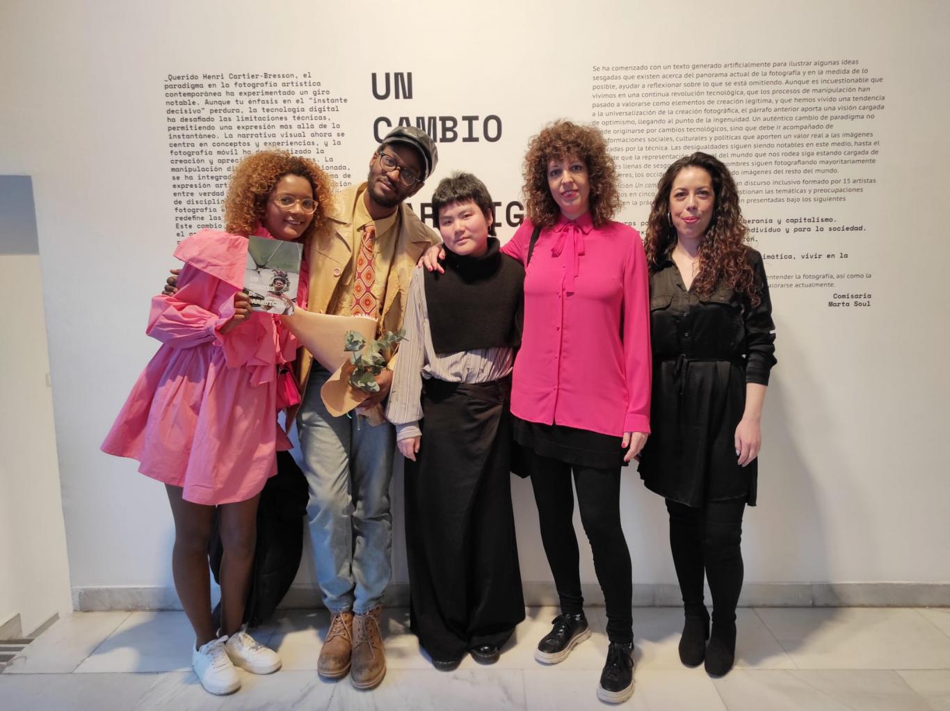 Group of young people posing in front of a text in an exhibition hall where the title of the exhibition is read A paradigm shift