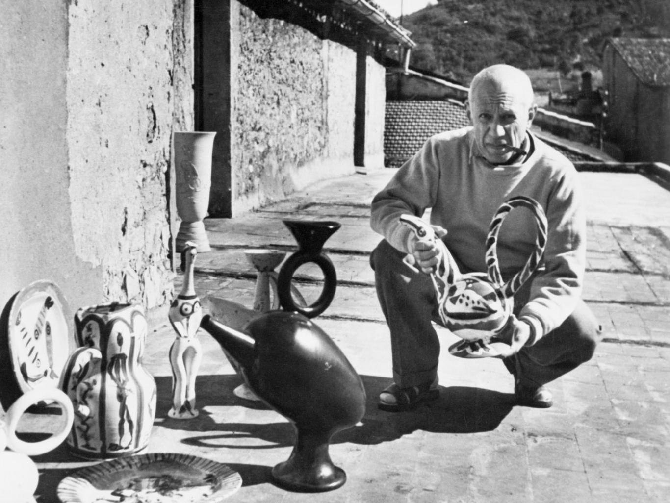 Picasso en cuclillas enseñando cerámicas al fotógrafo en el exterior de su estudio