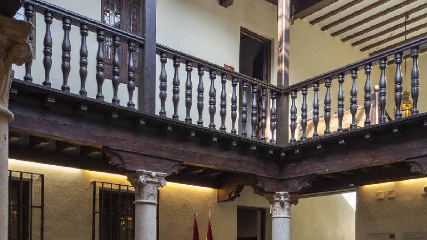 Vista de un patio interior con dos alturas y una barandilla de maderar en la planta superior