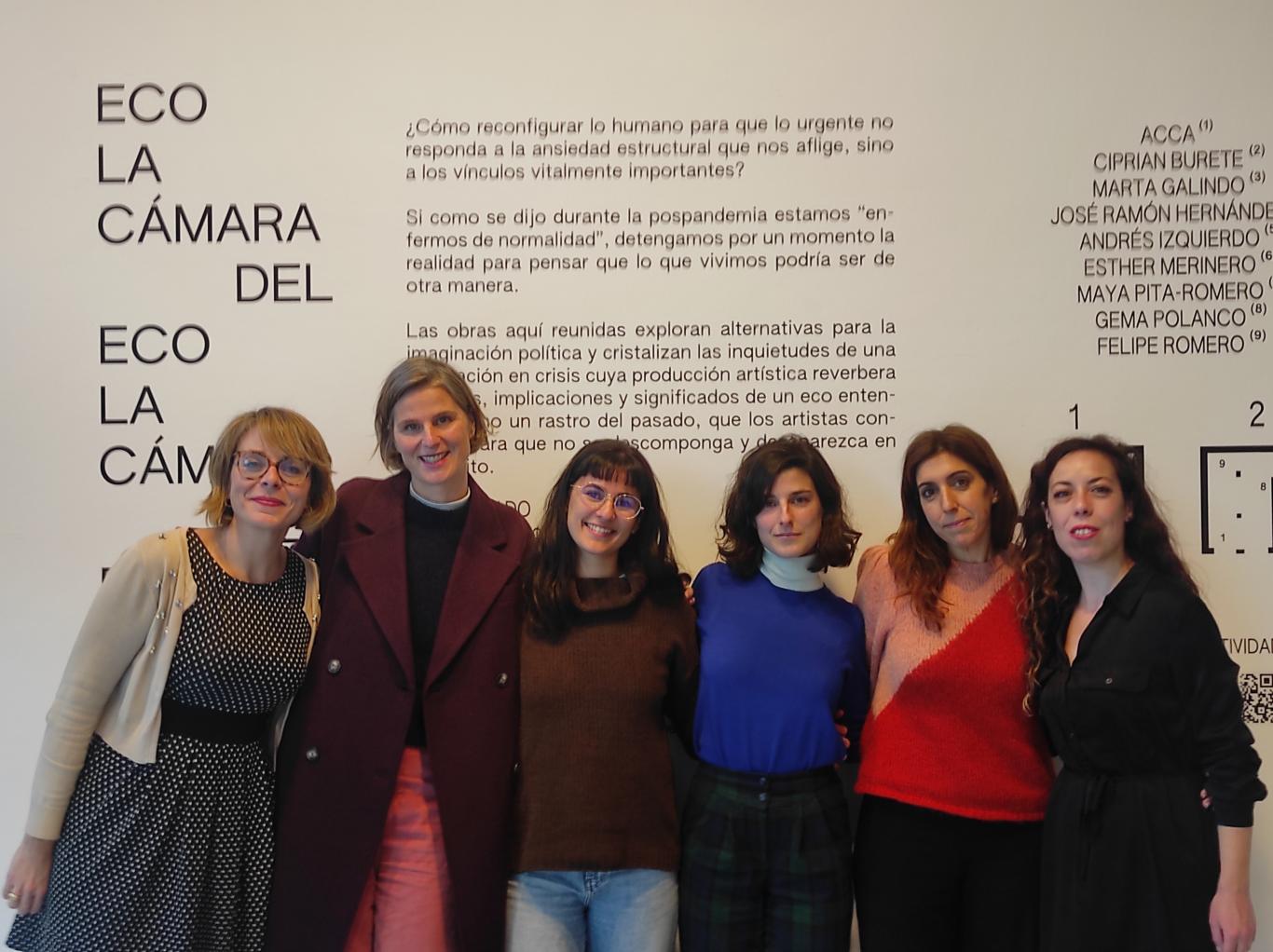 Group of women posing in front of a vinyl on the wall where the title of the exhibition appears
