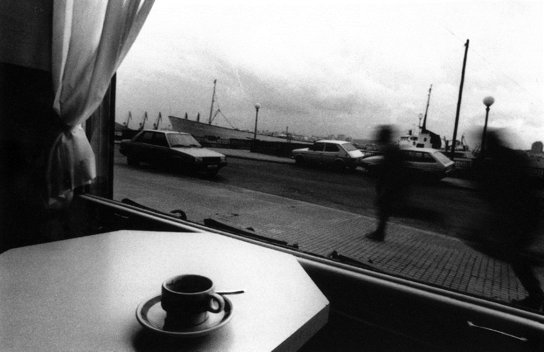 Foto en blanco y negro de una persona tomando un café y con una ventana con paisaje de fondo