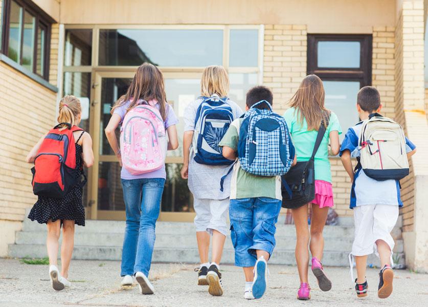 Colegiales con mochilas, de espaldas, a punto de entrar al colegio