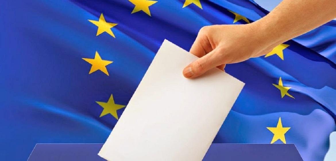 Mano depositando un voto, con bandera de la UE al fondo