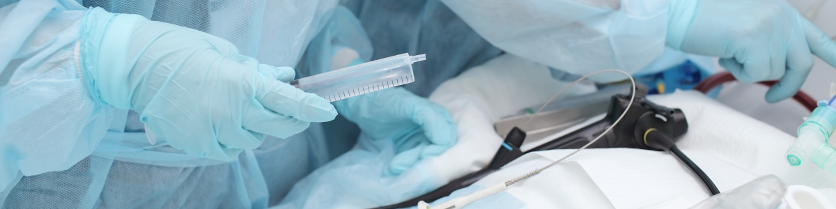 mesa de quirófano con sábana blanca y un aparato manual negro y manos de doctor con guantes azules y jeringa en la mano