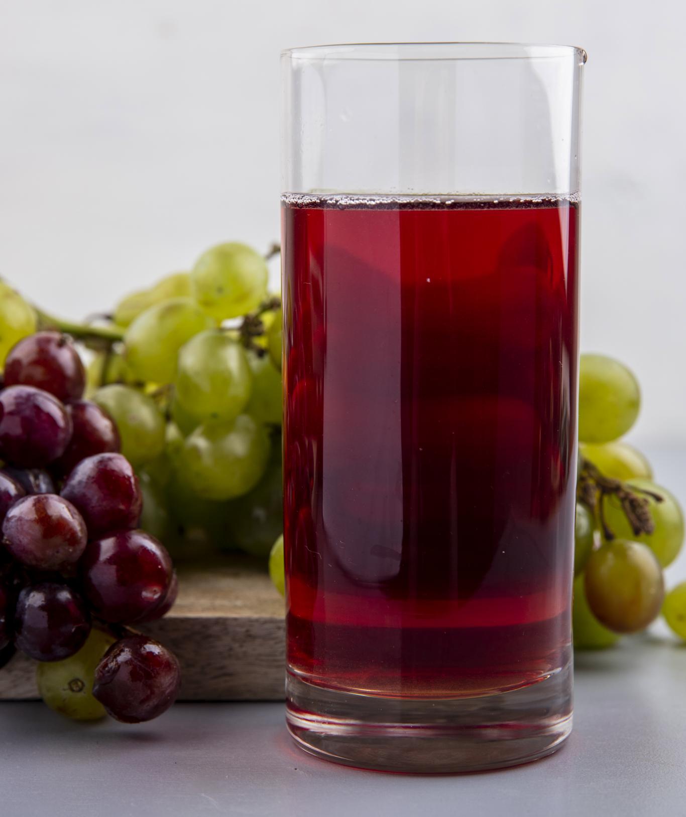 Vaso de zumo de uva en tabla de madera con racimos de uvas al fondo