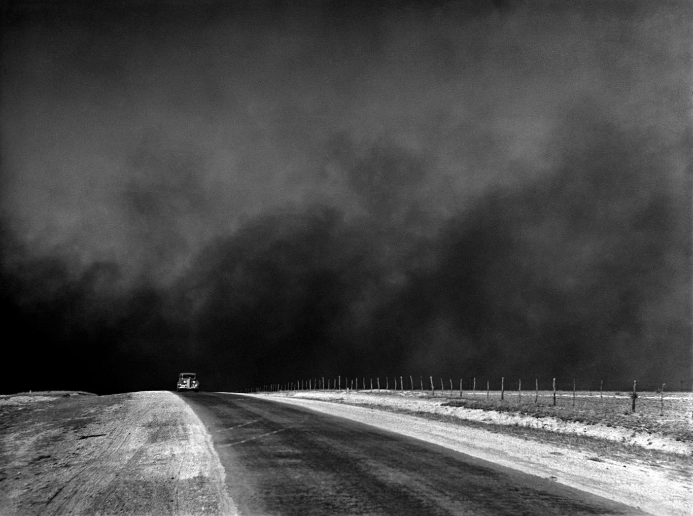 Imagen en blanco y negro de una carretera con un coche y el cielo lleno de polvo