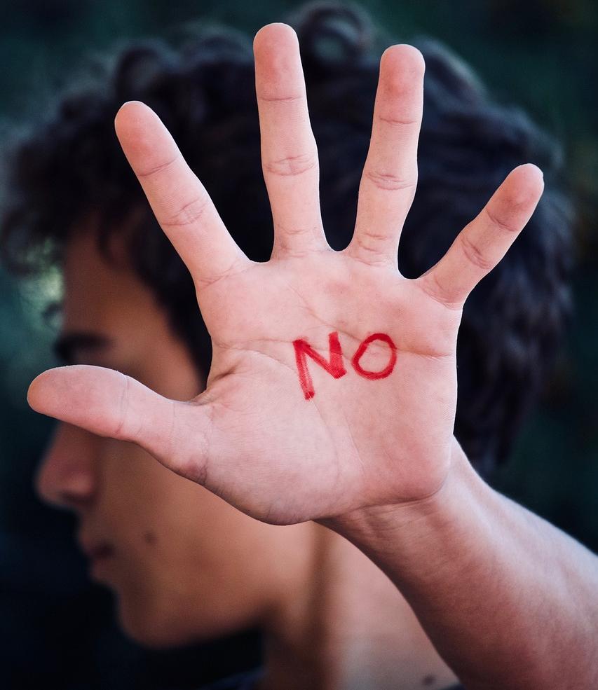Joven levantando la palma de la mano con la palabra NO
