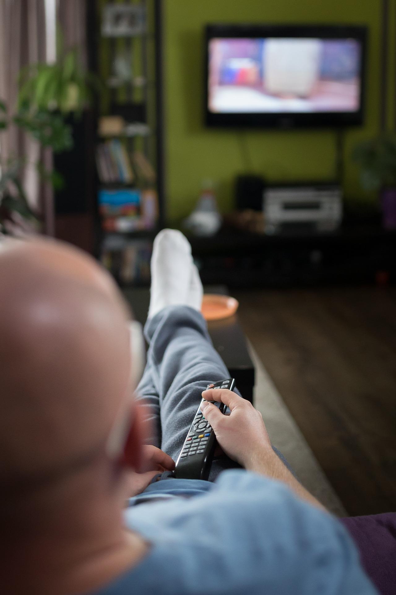 señor sentado en el sofá con el mando a distancia en la mano viendo la tv
