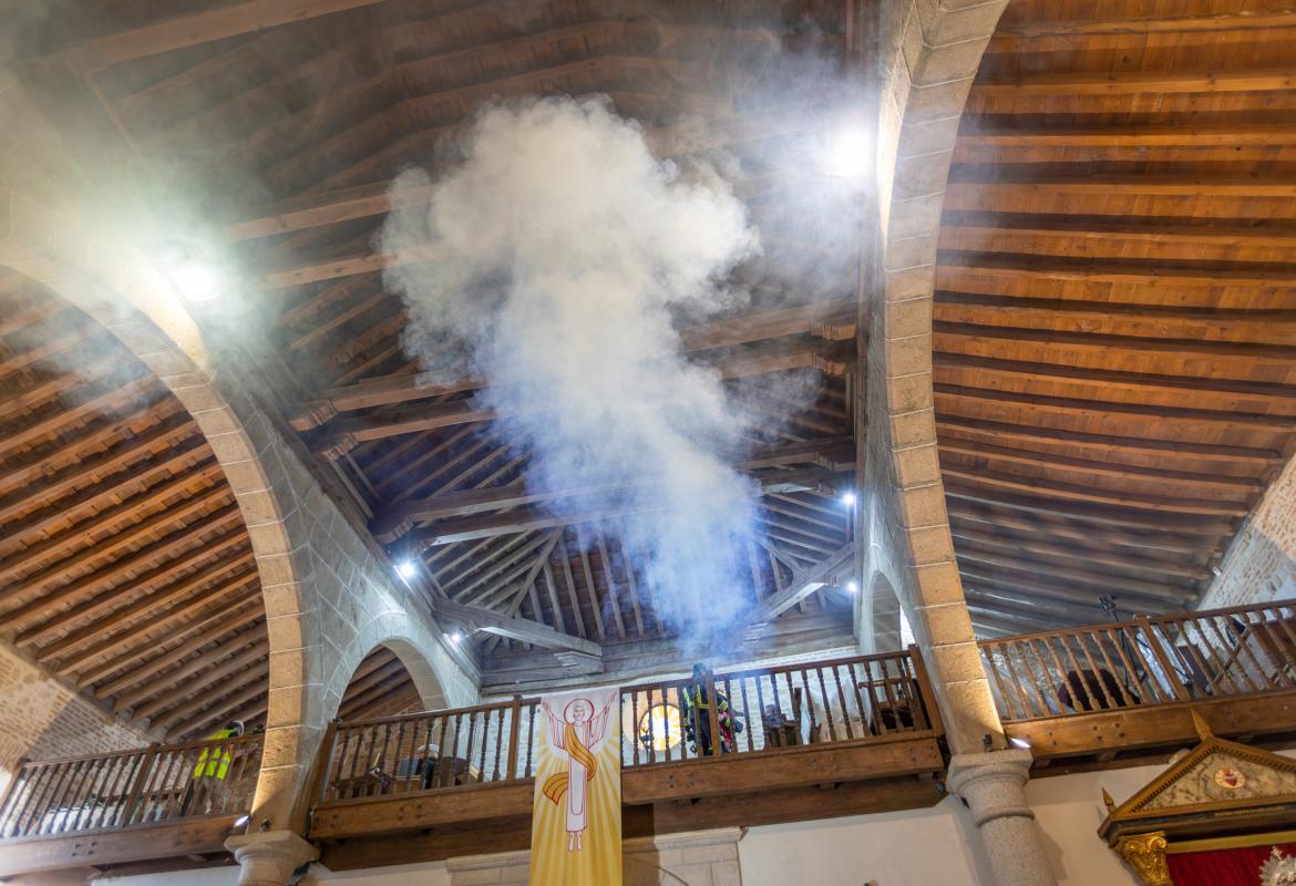 Humo en el interior de una iglesia con arcos de piedra y artesonado de madera