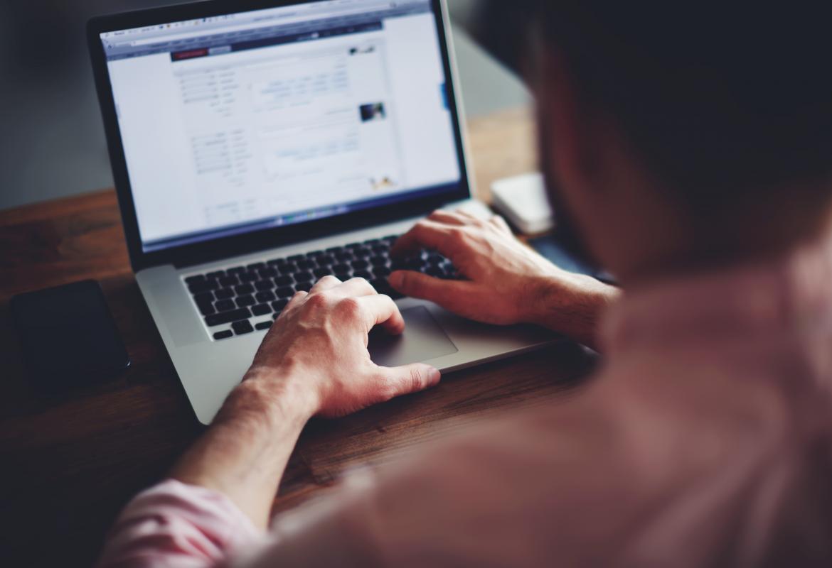 Man from behind, typing on a laptop