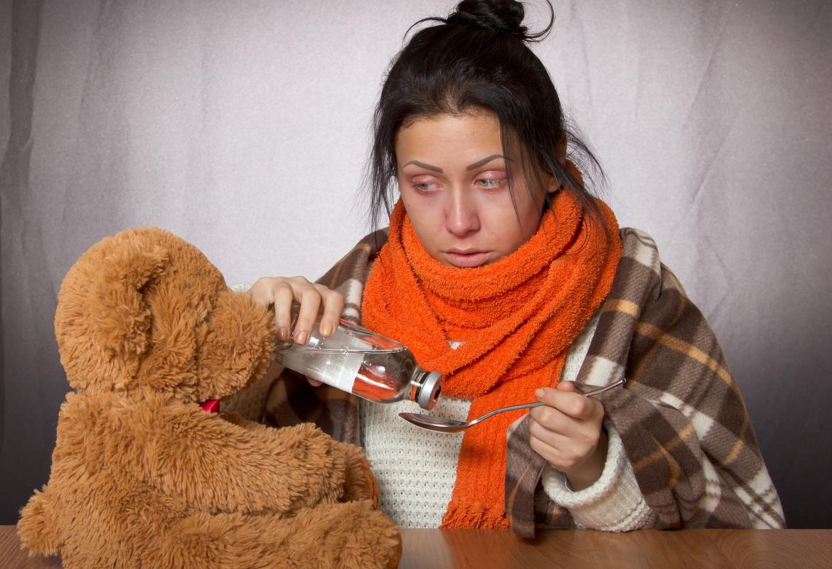 Mujer resfriada con bufanda y preparando toma de jarabe