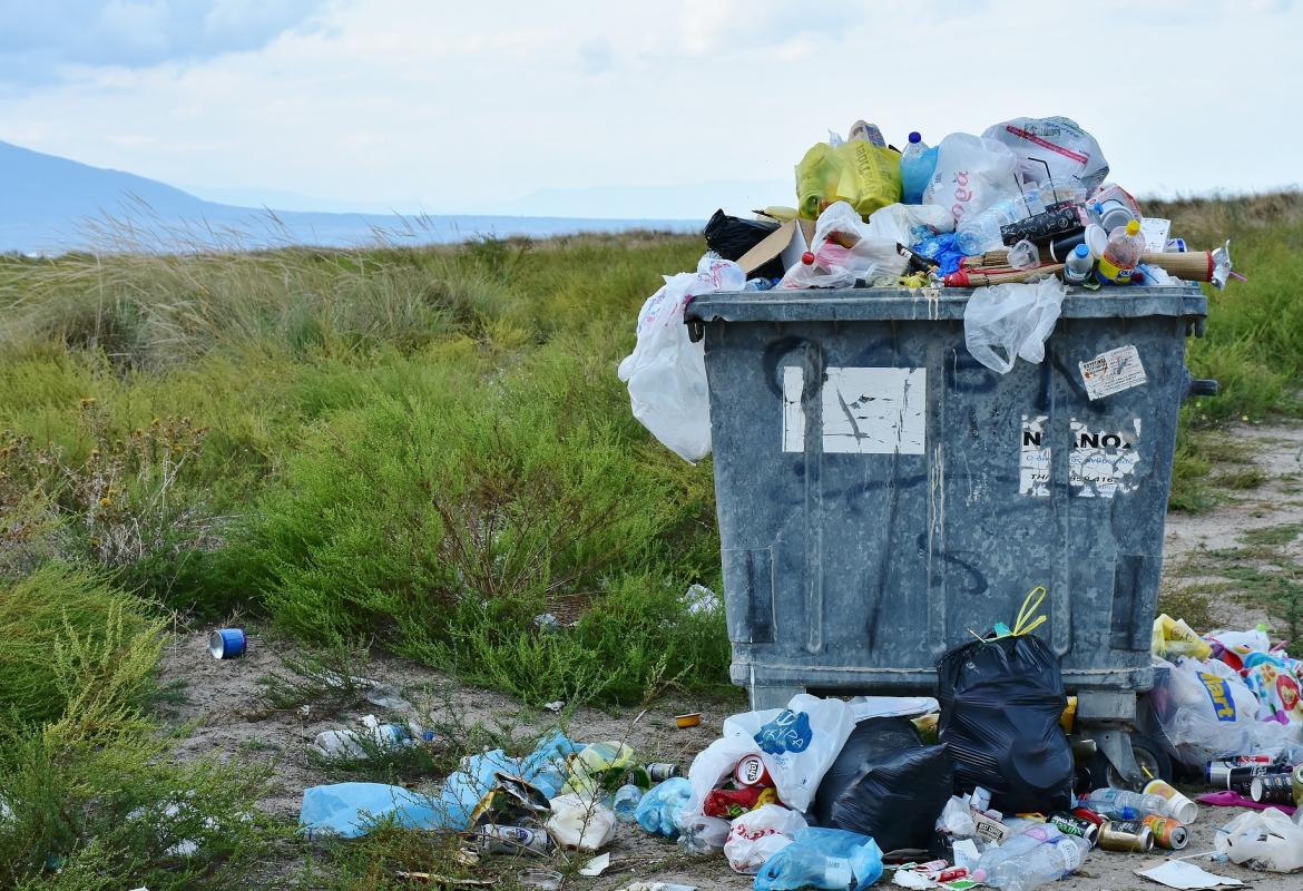 Contenedor de basura lleno y con bolsas rebosando y en el suelo