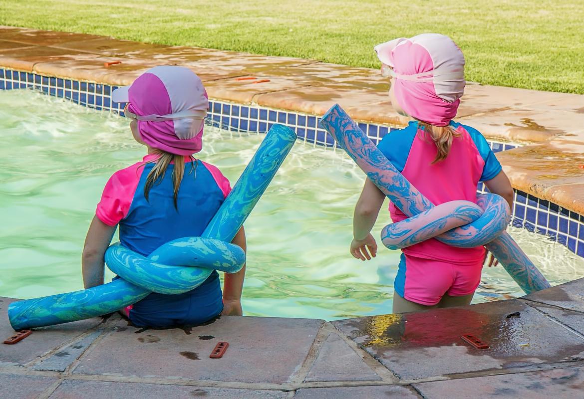 Dos niños de espalda en una piscina, con gorro y flotador