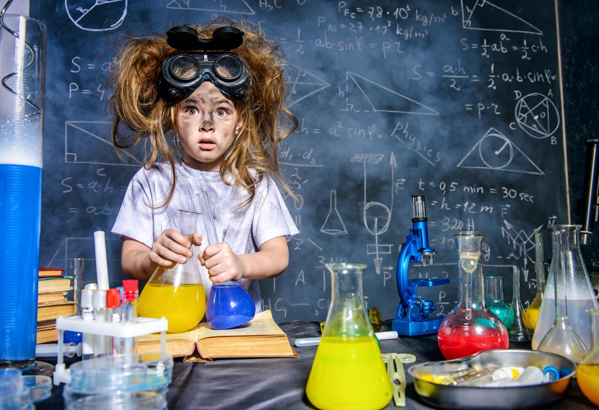 Niña con la cara sucia, gafas de laboratorio en la cabeza y pelos alborotados con matraces en la mano en un laboratorio