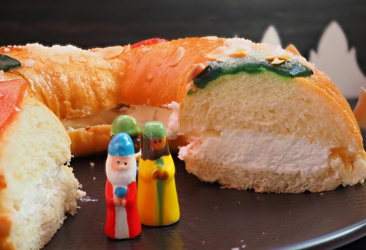 Roscón de nata con un trozo cortado y con 3 figuritas de Reyes Magos en el hueco