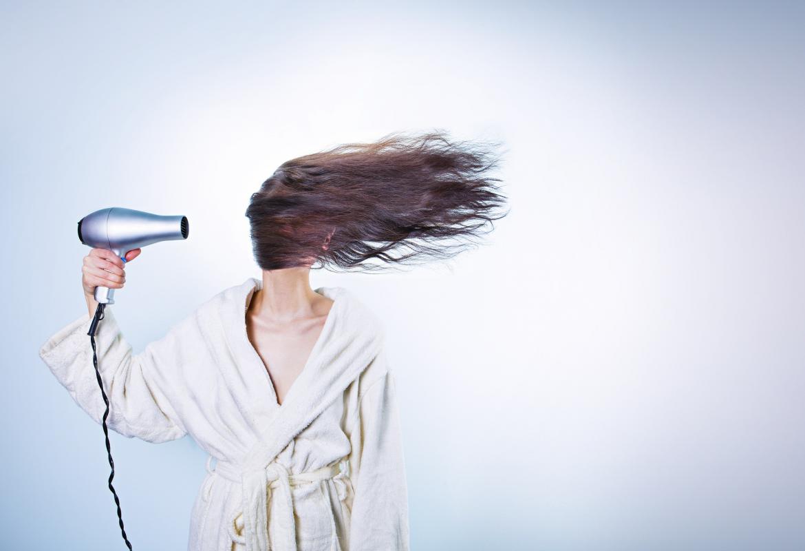 Chica en bata secándose el pelo con un secador de mano