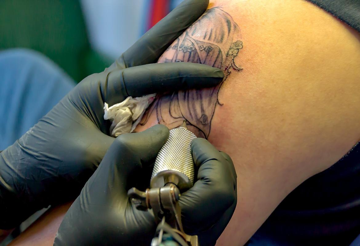 Manos de un tatuador, con guantes, realizando un tatuaje en un brazo