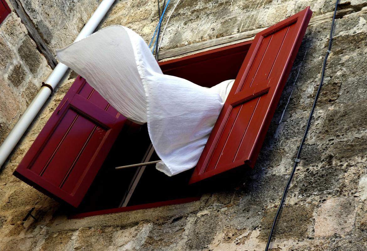 Fachada de una casa antigua con las ventanas abiertas y la cortina moviéndose por el viento