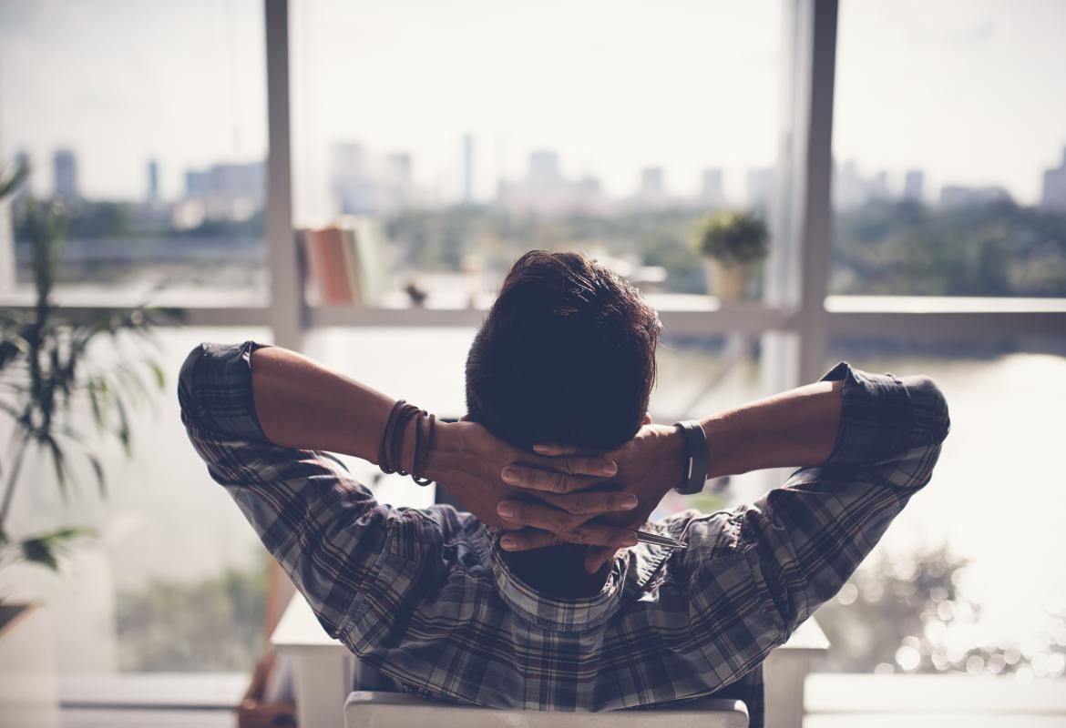 hombre relajado sentado mirando hacia la ventana con las manos entrelazadas detrás de la cabeza