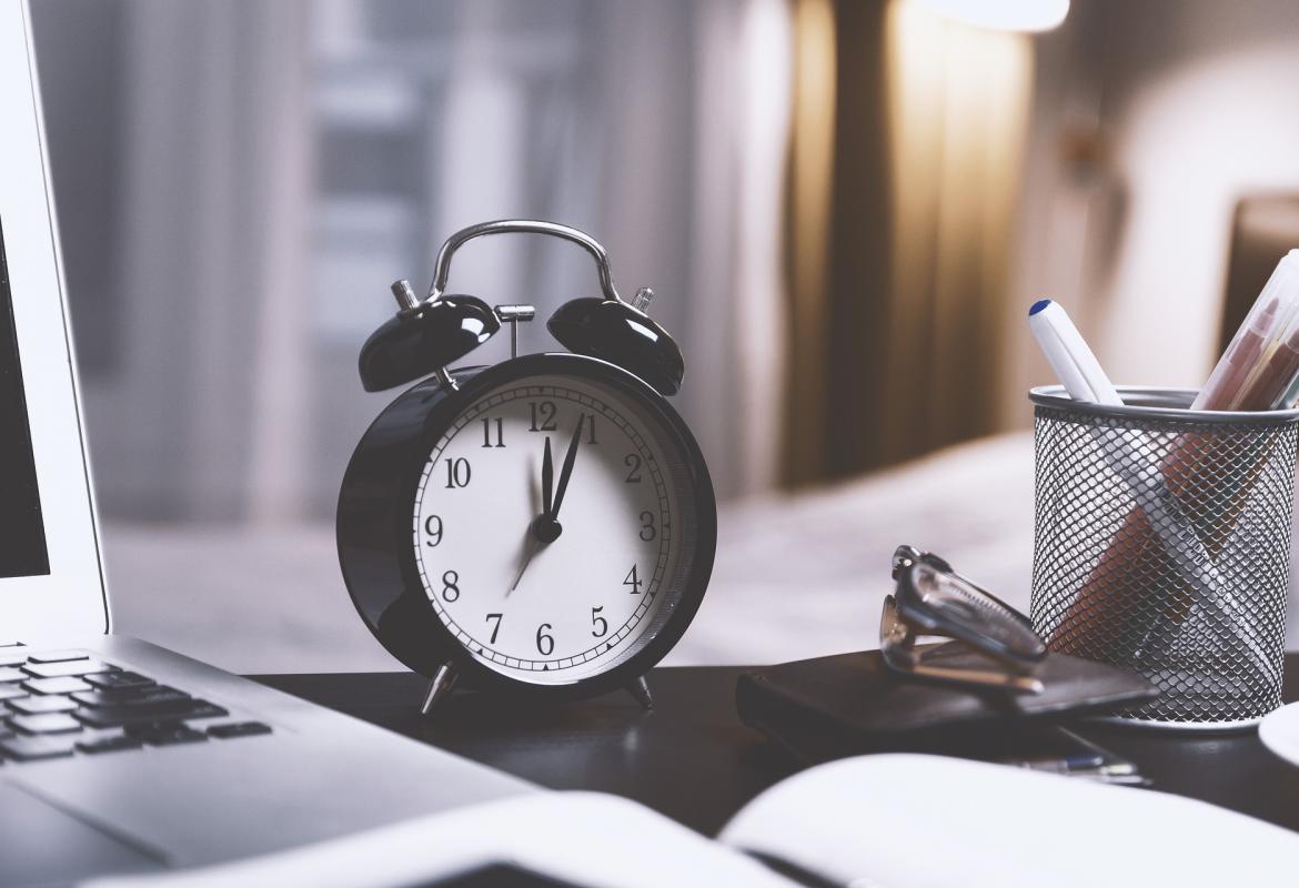 reloj sobre una mesa al lado de un ordenador, unas gafas y bolígrafos