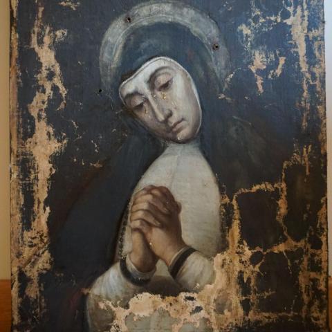 imagen de una pintura deteriorada representando a la virgen en posición de oración llorando y vistiendo corona de plata